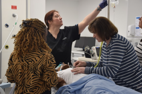 Three people standing around a bed